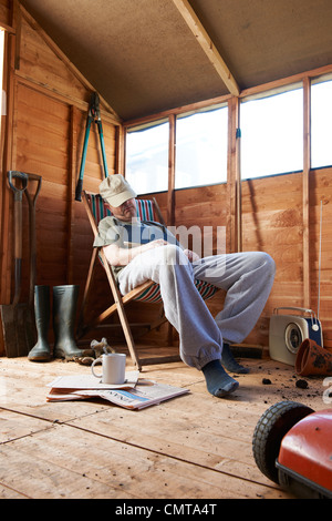Man sitting in deckchair falling asleep in the shed while reading book Stock Photo