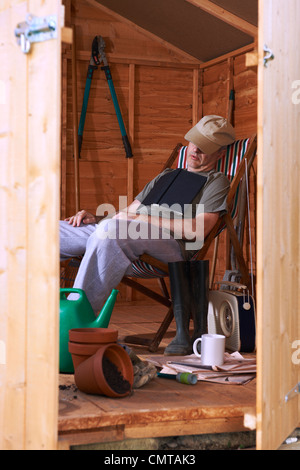 Man sitting in deckchair falling asleep in the shed while reading book Stock Photo