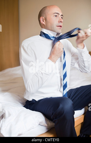 Man adjusting tie while sitting on bed Stock Photo