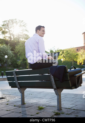 Smiling businessman sitting on bench and using laptop Stock Photo