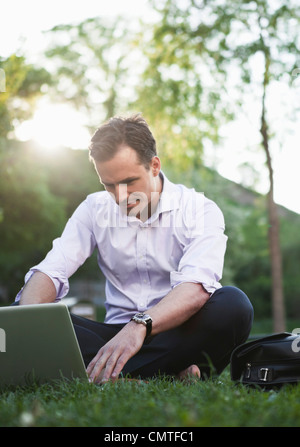 Man sitting on grass and using laptop Stock Photo