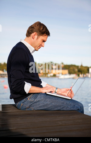 Concentrated man using laptop while sitting on jetty Stock Photo
