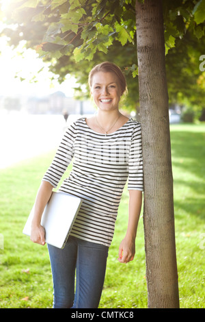 Happy woman leaning against tree Stock Photo