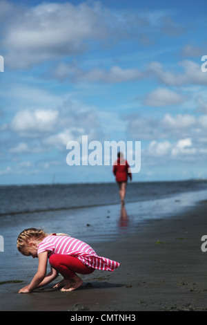 Girl (4-5) playing with sand with mother in the background at beach