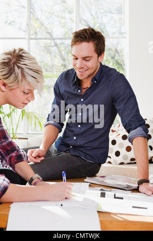 Man sitting on table, looking at woman writing Stock Photo