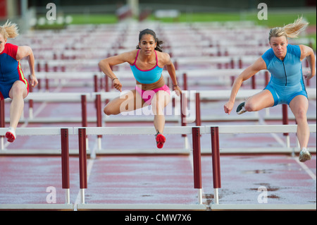 Runners jumping hurdles in race Stock Photo
