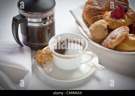 breakfast cup of white coffee and cafetiere and with pastries , laid out on a white linen tablecloth Stock Photo