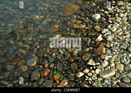 A close up image of pebbles on a beach with water covering some. Stock Photo