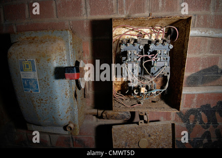 A broken down and decrepit old electrical panel box on the wall of an abandoned industrial factory. Stock Photo