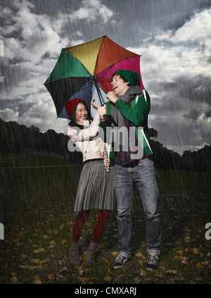 Germany, Cologne, Young couple with umbrella in park, smiling Stock Photo