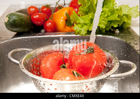 Three fresh tomatoes in colander splashing in water Stock Photo