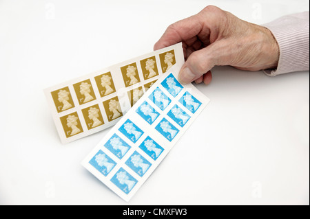 Elderly woman holding a book of 1st first & 2nd second class stamps Stock Photo