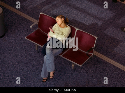Woman passenger asleep in the seating area of departure lounge at Heathrow airport Stock Photo