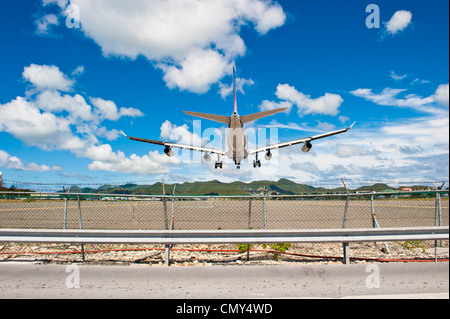 A centered shot of an airplane landing on a runway near grassy mountains, on a sunny, cloudy day. Stock Photo