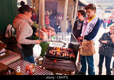 Young woman stall holder cooking sausages at Saturday Farmers Market in Stroud, Gloucestershire, UK Stock Photo