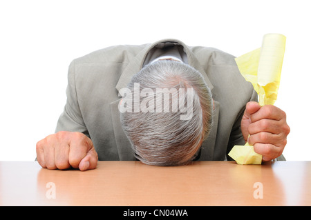 A frustrated businessman with his head on his desk and a piece of crumpled paper in one hand. Stock Photo