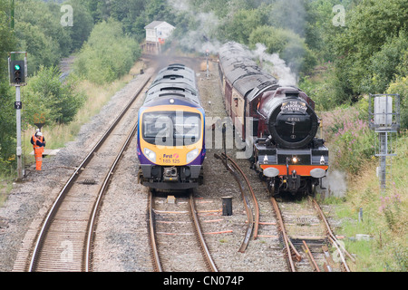 Steam locomotive pulling a passenger train on the main line and passing a diesel passenger train on the Pennine route Stock Photo