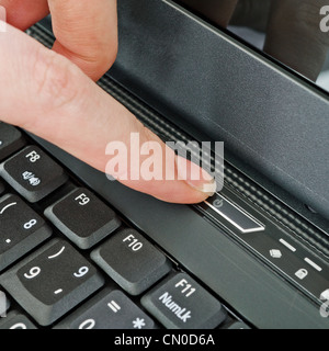 female finger pressing power key on the laptop, selective focus on key-press Stock Photo