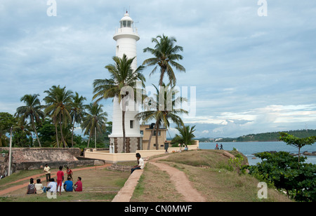 Local families play cricket beneath the lighthouse of Galle Fort Sri Lanka Stock Photo