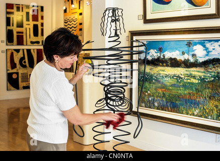 Female Art Gallery Owner Dusting Sculpture Stock Photo
