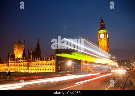 Big Ben Clock Tower Houses of Parliament at night with blurred lights of passing red London bus in foreground London England UK Stock Photo