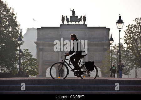 An early morning commuter cycles past the Arc de Triomphe du Carrousel in Jardin desTuileries, Paris, France. Stock Photo