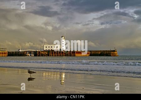 Scarborough Lighthouse, harbour entrance and sea wall bathed in an early winter evening light as the tide ebbs with majestic clouds over the North Sea Stock Photo