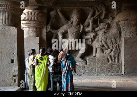 Indian tourists watching a stone carving depicting Shiva slaying the Andhaka demon. Cave nº 29. Ellora caves. India Stock Photo
