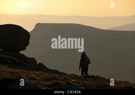 A walker on the edge of the Kinder Scout plateau above Edale, Peak District, Derbyshire, England, UK. Crowden Tower behind. Stock Photo