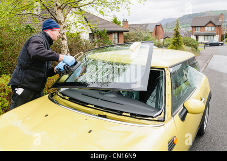 Man fits a new windscreen to a yellow car Stock Photo