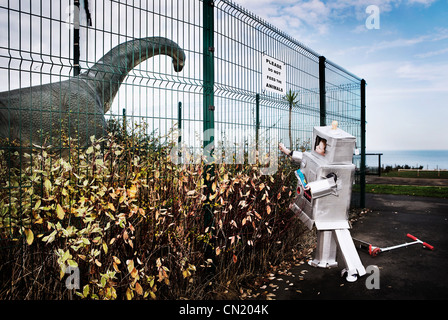 Boy dressed as robot feeding model dinosaur crisps through fence Stock Photo