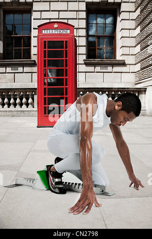 Olympic sprinter on starting line with red telephone box in background Stock Photo