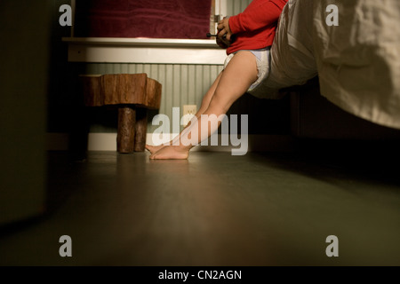 Toddler boy leaning against bed Stock Photo