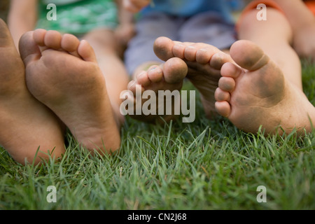 Three children sitting on grass with dirty feet Stock Photo