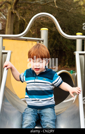 Portrait of a two year old boy going down a slide in a playground Stock Photo