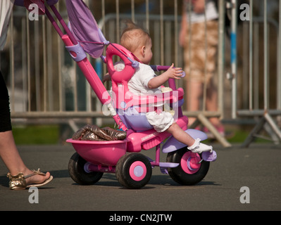 A baby being pushed along in a very pink tricycle seat or pushchair Stock Photo