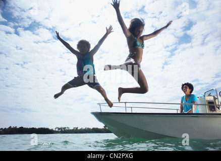 Mother on motorboat, two children jumping into water Stock Photo
