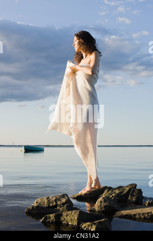 Woman wrapped in blanket standing by sea Stock Photo