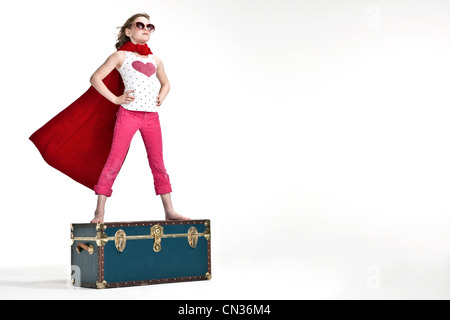 Girl standing on trunk suitcase dressed as superhero Stock Photo