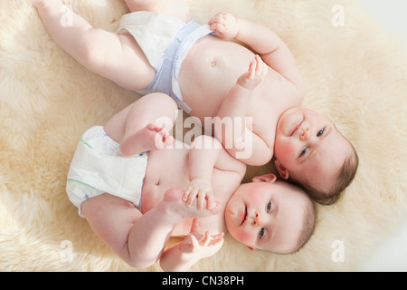 Twin baby girls lying on a sheepskin rug Stock Photo