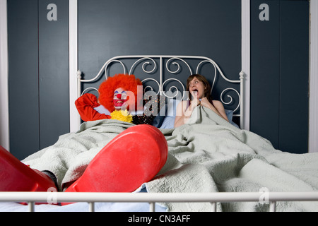 Woman screaming as she realises she is in bed with a clown Stock Photo