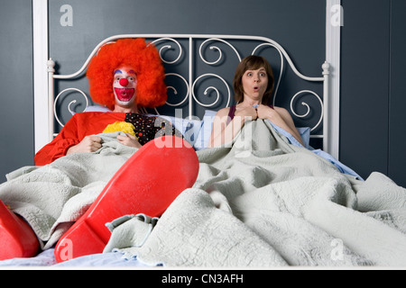 Clown and woman surprised to find themselves in bed together Stock Photo