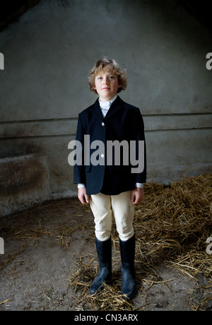 Boy standing in horse riding clothes in stable Stock Photo