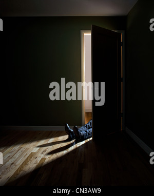 Businessman lying in doorway of dark room Stock Photo