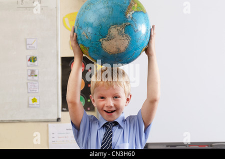 School boy holding globe over his head in a classroom Stock Photo