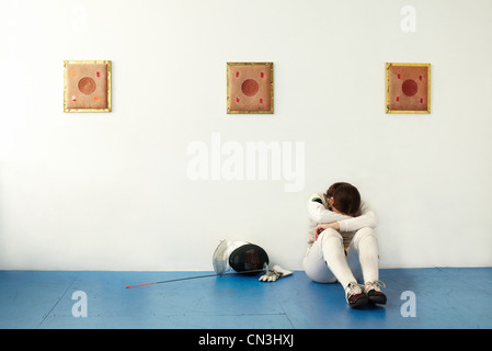 Female fencer sitting against wall with head in hands Stock Photo