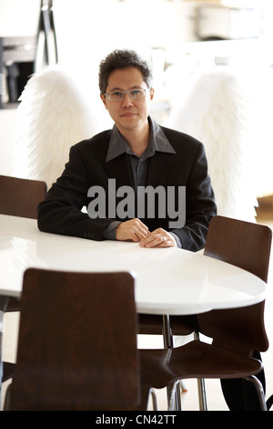 Man Wearing a Business Suit with Wings Sitting at a White Table, Montreal, Quebec Stock Photo