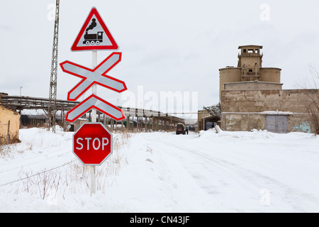 Stop sign before the railway crossing, winter season in Russia. Industrial plant Stock Photo