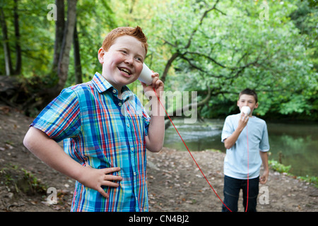 Two boys using paper cups and string to communicate in woodland Stock Photo