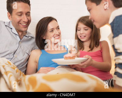 Mid adult woman receiving birthday cake in bed from family Stock Photo